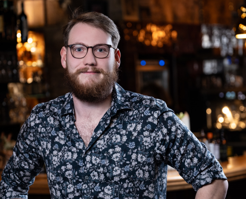 Mitarbeiterporträt eines Mannes mit Brille und Bart im Innenbereich